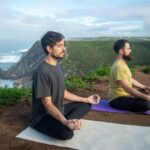 Home Two men practicing meditation on yoga mats overlooking a scenic cliff in Portugal.